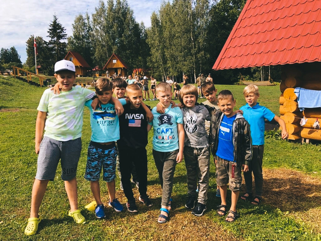 Вожатая обнимает ребёнка на фоне зелёной поляны в детском лагере